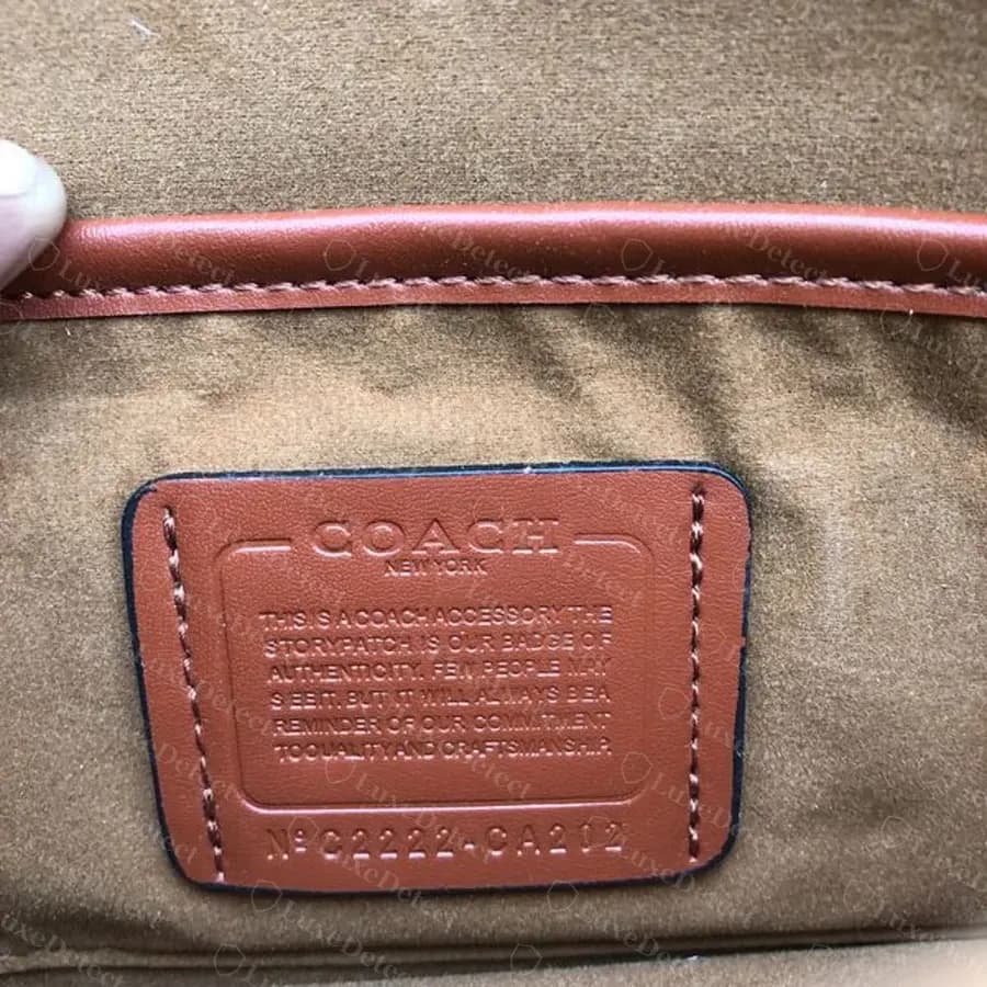 Parche del creed dentro de un bolso de hombro Tabby negro falsificado y confirmado: texto "This is a Coach accessory", palabras pegadas en la última línea y código N° C2222-CA202.