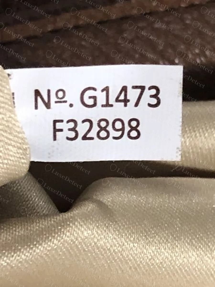 A white fabric tag inside a genuine Coach bag printed N. G1473 over F32898, which reads July 2014, factory 73, outlet style F32898