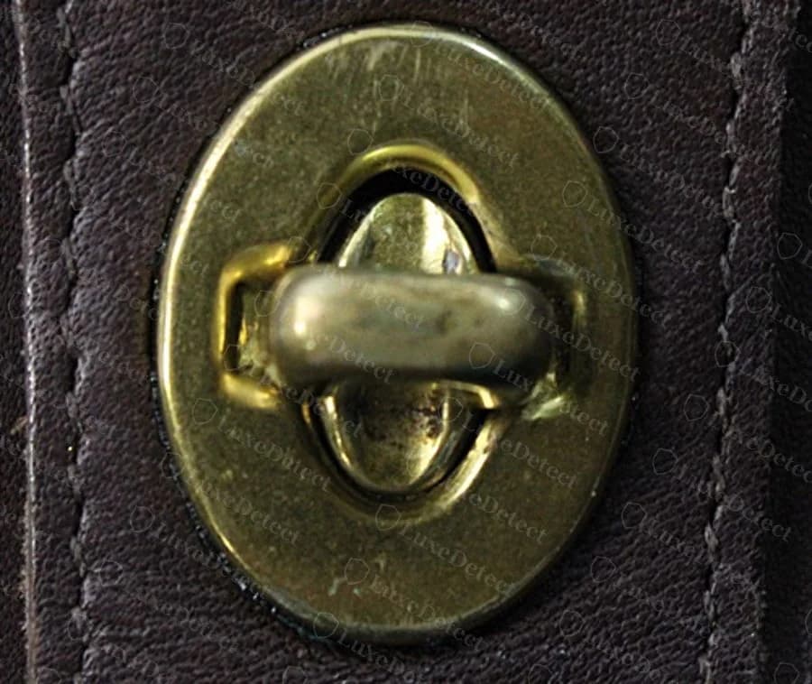 Close-up of the oval turnlock on a verified authentic Willis, showing the brass casting and rivet stitching around the mounting plate.
