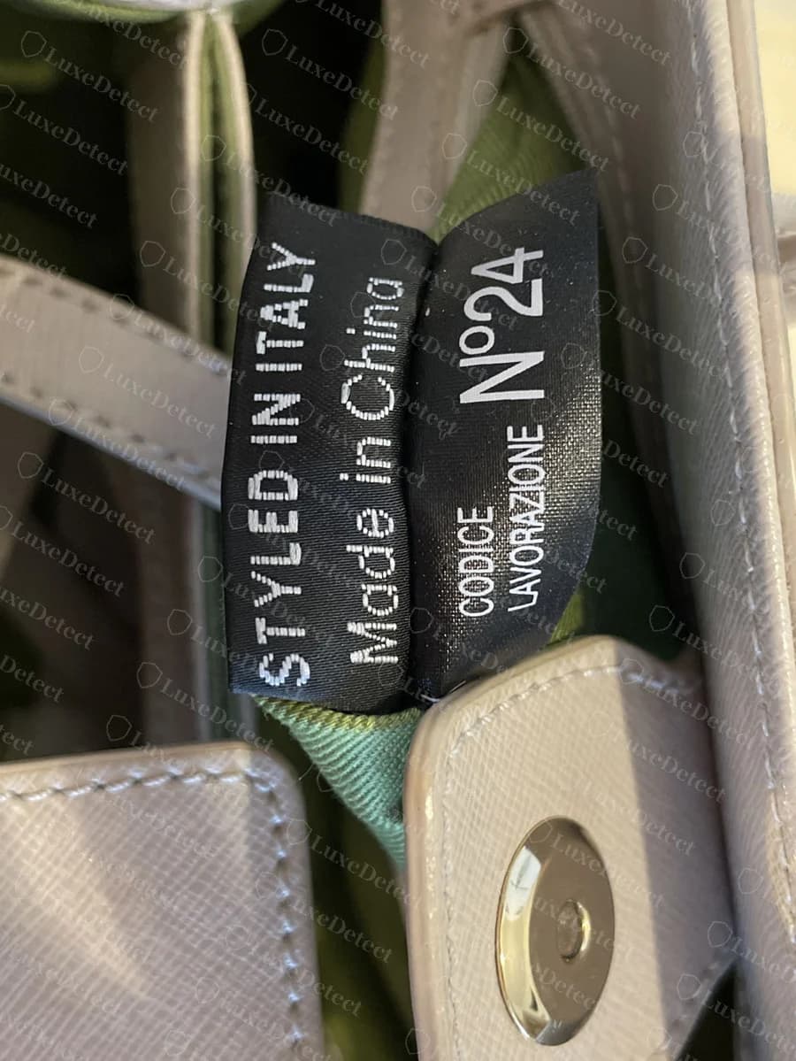 Genuine Coccinelle pair of black woven tags, one reading STYLED IN ITALY and Made in China, the other CODICE LAVORAZIONE N°24, hanging inside a taupe saffiano bag