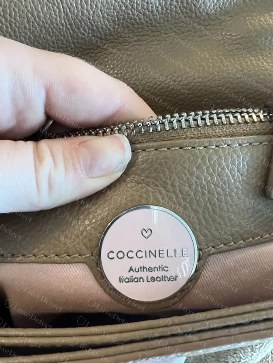 Genuine Coccinelle round pink enamel disc with a small heart, COCCINELLE and Authentic Italian Leather, set on a tan leather pocket above a pink lining