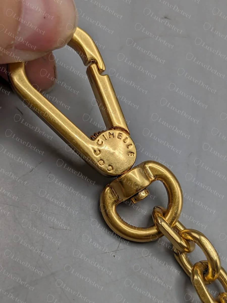 Genuine Coccinelle gold-tone lobster clasp with COCCINELLE engraved around the curved face, joined to a chain strap