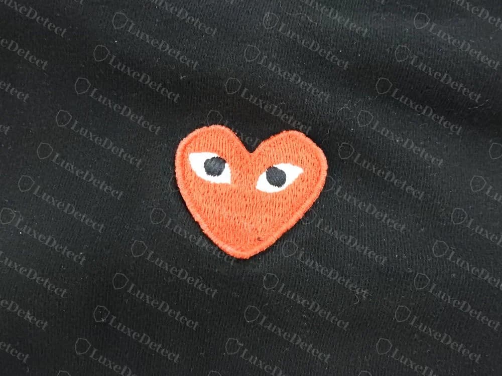 Corazón rojo bordado genuino de PLAY en una camiseta negra, un parche compacto con relleno apretado, borde satinado y dos ojos blancos con pupilas negras
