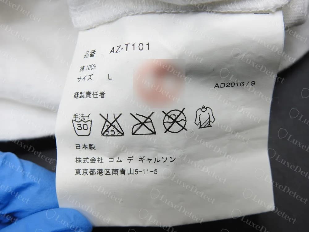 Genuine PLAY Japanese care tag: style code AZ-T101, 100 percent cotton, size L, season code AD2016/9, wash symbols, made in Japan and the Comme des Garçons Co., Ltd. address, with the red hanko stamp blurred