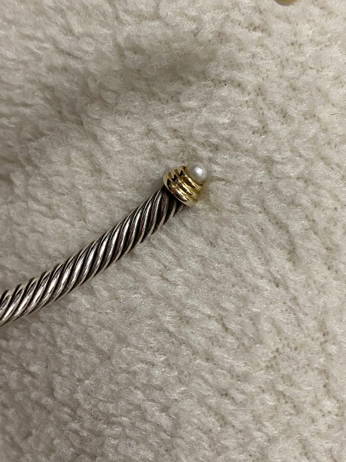 Remate David Yurman falsificado: un remate de oro mal fundido con una perla engastada torcida y descentrada, un tono oscuro y oxidado, y un trenzado de cable suelto y estirado que entra en él