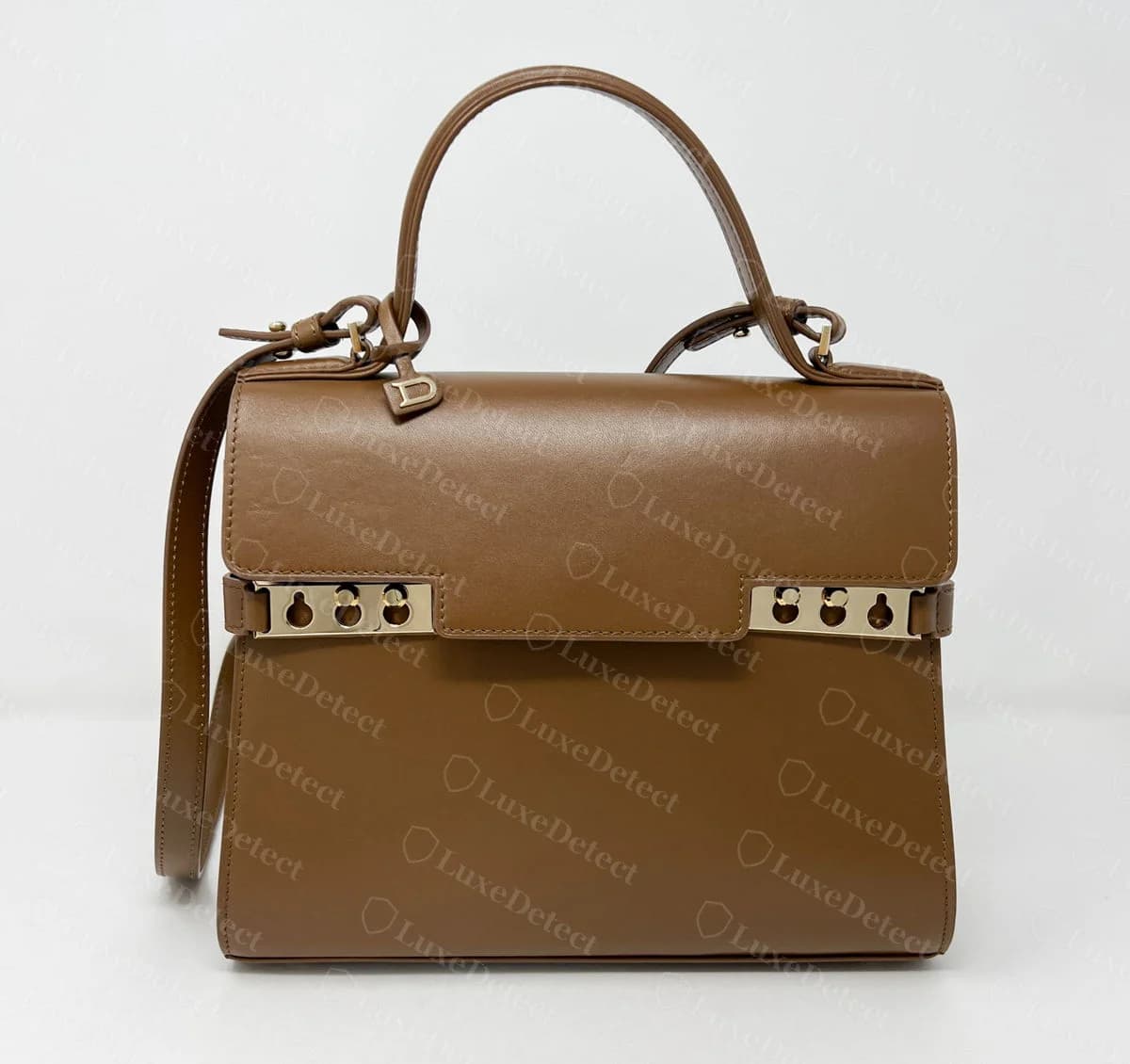 Counterfeit Delvaux Tempête in brown leather with gold-tone side plates, D charm and shoulder strap, closely matching the genuine silhouette