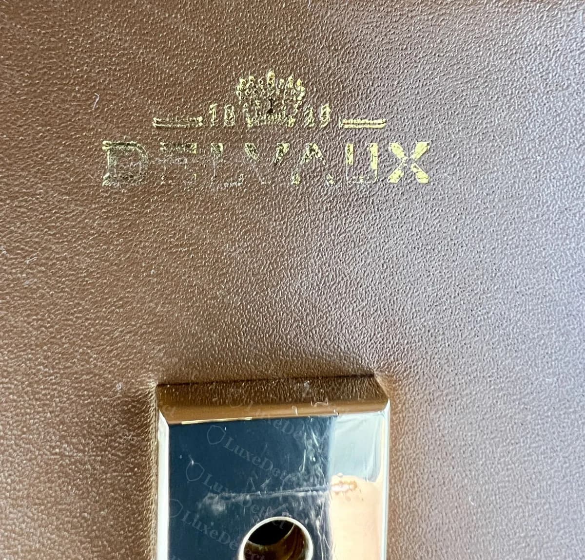 Counterfeit Delvaux Tempête logo stamp with patchy, partly filled gold foil on DELVAUX, above the lock plate