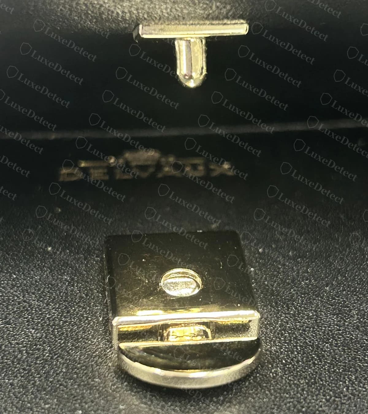 Genuine Delvaux Tempête closure, with the post plate on the underside of the flap above a square lock plate with a round opening and a hinged half-round tab
