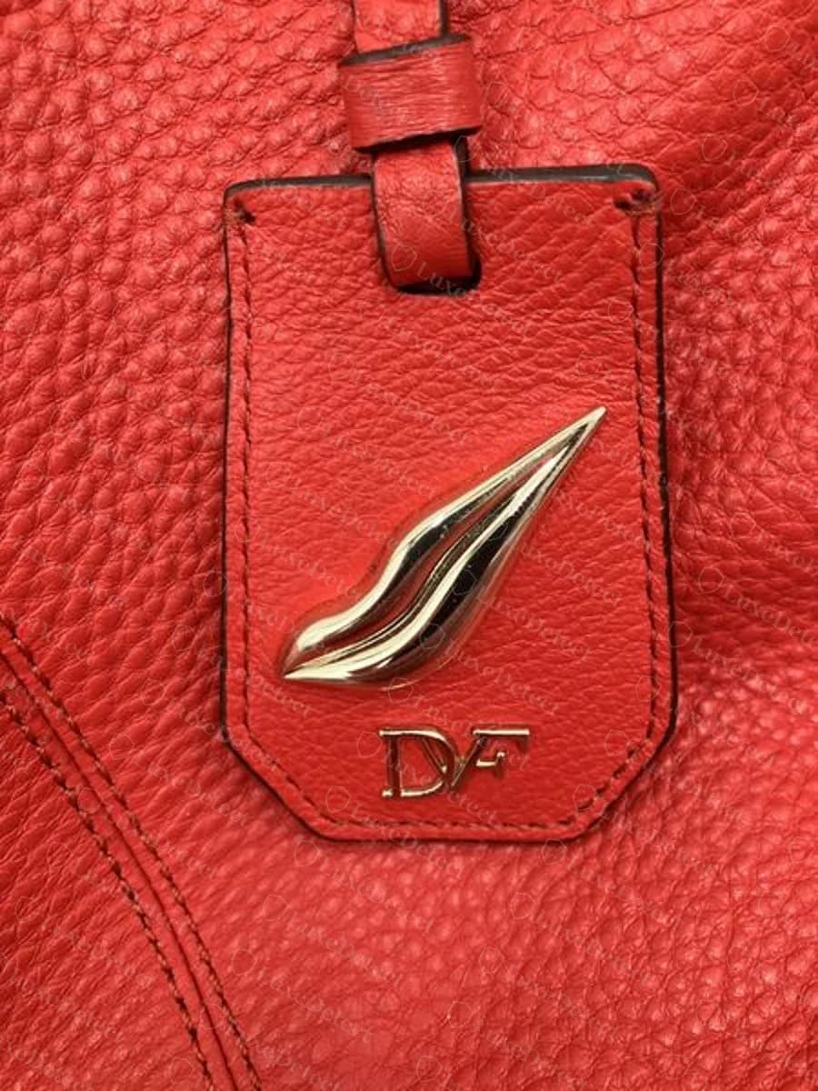 Genuine Diane von Furstenberg red pebbled leather tab holding a polished lip-shaped metal charm above a gold-tone DVF plate, on a satchel