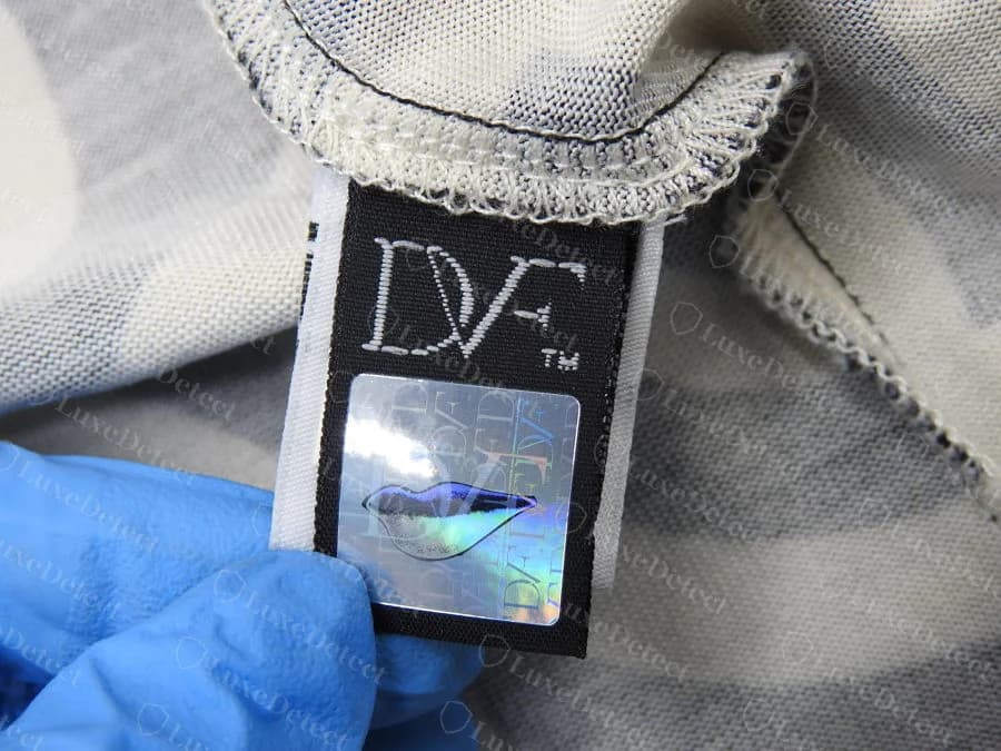 Genuine Diane von Furstenberg black woven neck label reading DVF with a trademark sign, with a square silver hologram sticker below, sewn into the neckline of a silk jersey wrap dress