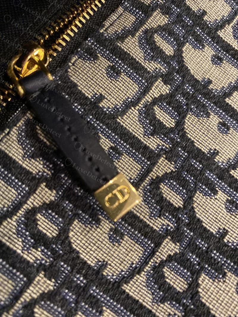 Interior zipper pull stamped with a small "CD" monogram against the oblique jacquard lining