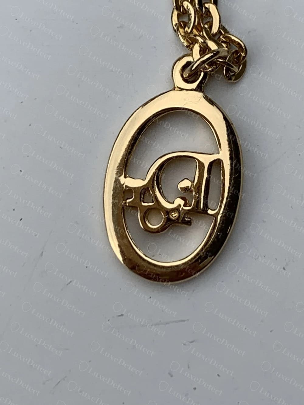 Counterfeit Dior CD-clasp pendant with visibly uneven, slightly melted-looking edges on the oval cutout, and no engraved wordmark on the bar at all