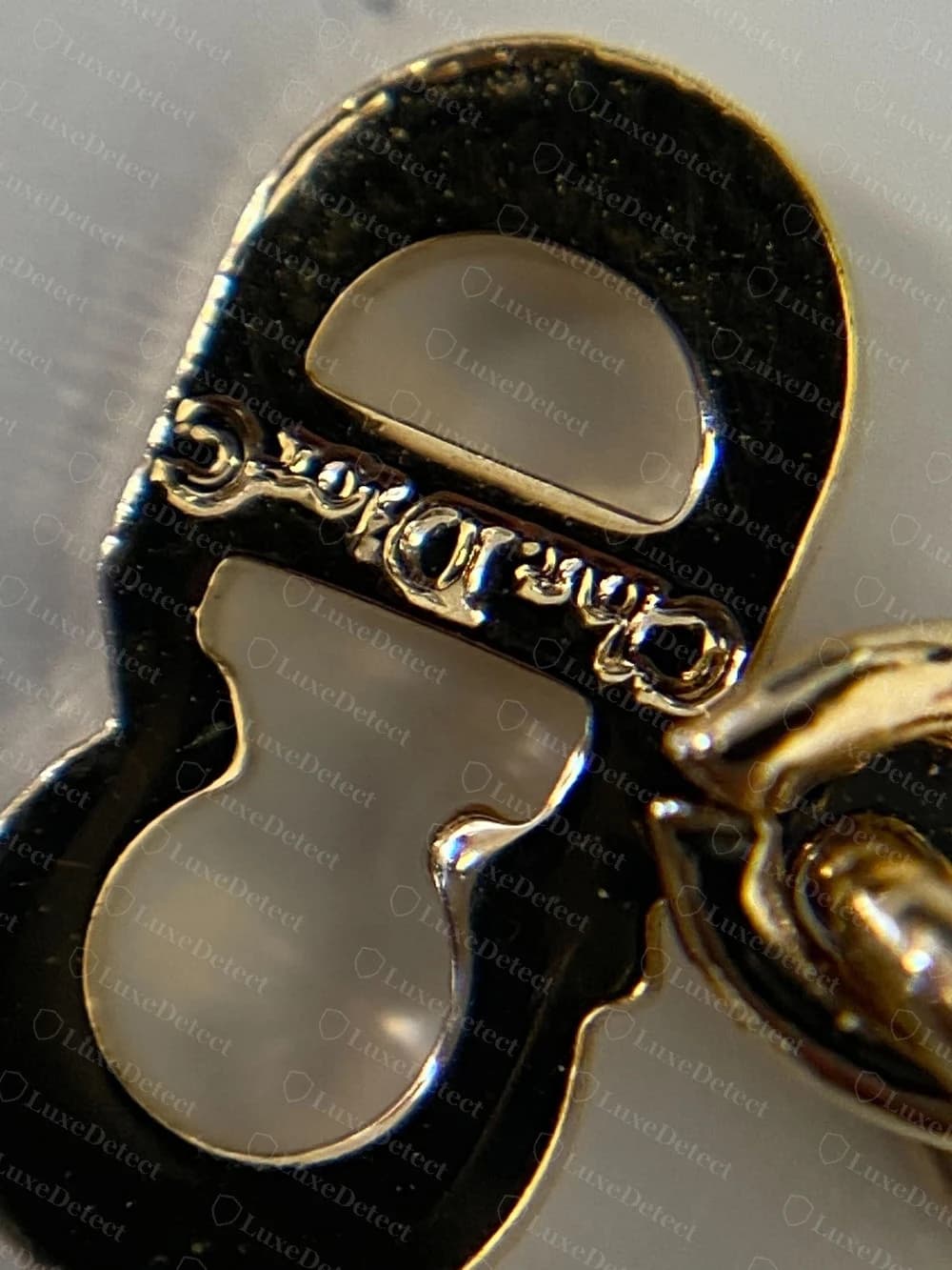 Counterfeit Dior CD-clasp charm with a shallow, blurred engraving on the connecting bar, letterforms barely legible even at macro range