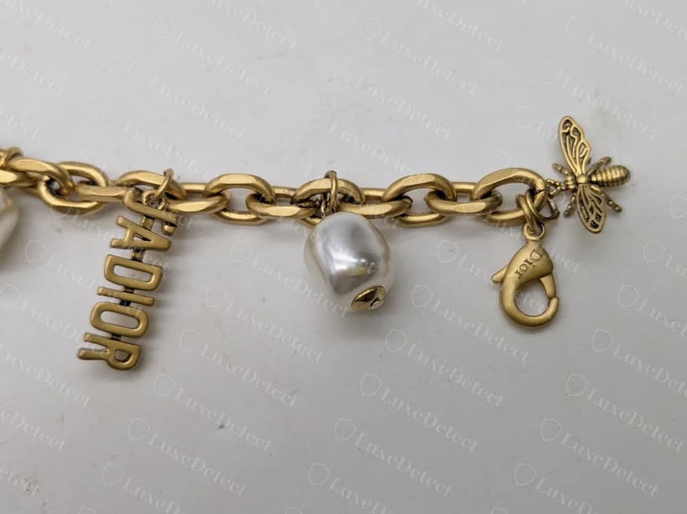 Authentic Dior J'Adior pearl charm bracelet: the "J'ADIOR" letter charm, a baroque faux pearl, a bee charm, and a lobster clasp engraved "Dior" in upper-and-lowercase script