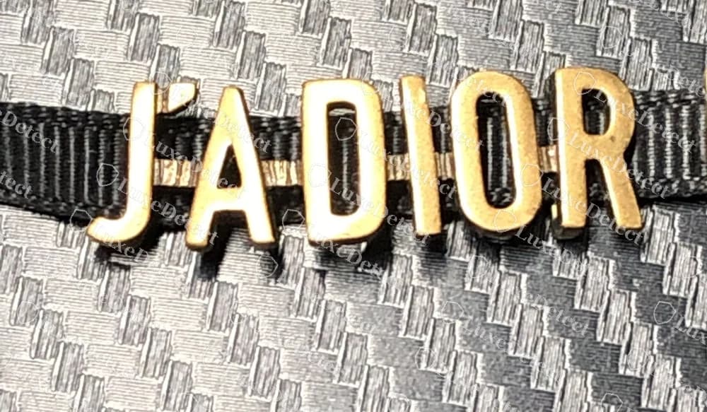 Gefälschtes Dior J'Adior Halsband aus Band, dessen Buchstabenguss die echte Schrift eng kopiert, mit Fahnen-J, separatem Apostroph und dünn-dickem A