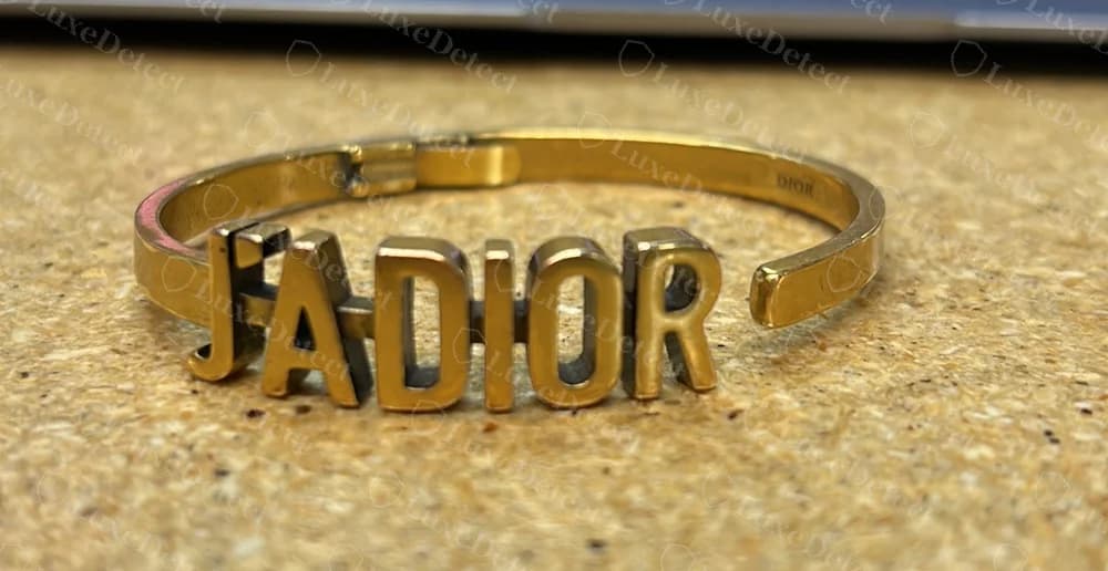 Echte Dior J'Adior Scharniermanschette mit den Buchstaben „J'ADIOR“, als einzelne, erhabene Großbuchstaben gegossen und durch einen dünnen Steg verbunden, mit einem kleinen Stempel „DIOR“ an der Innenseite des Bandes