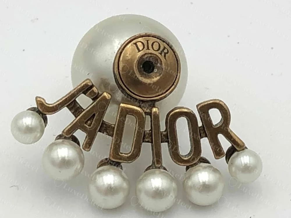 Pendiente de perla J'Adior de Dior original: letras "J'ADIOR" con una pequeña perla colgando bajo cada una, y un sello "DIOR" en mayúsculas en la copa redonda trasera detrás de la perla grande