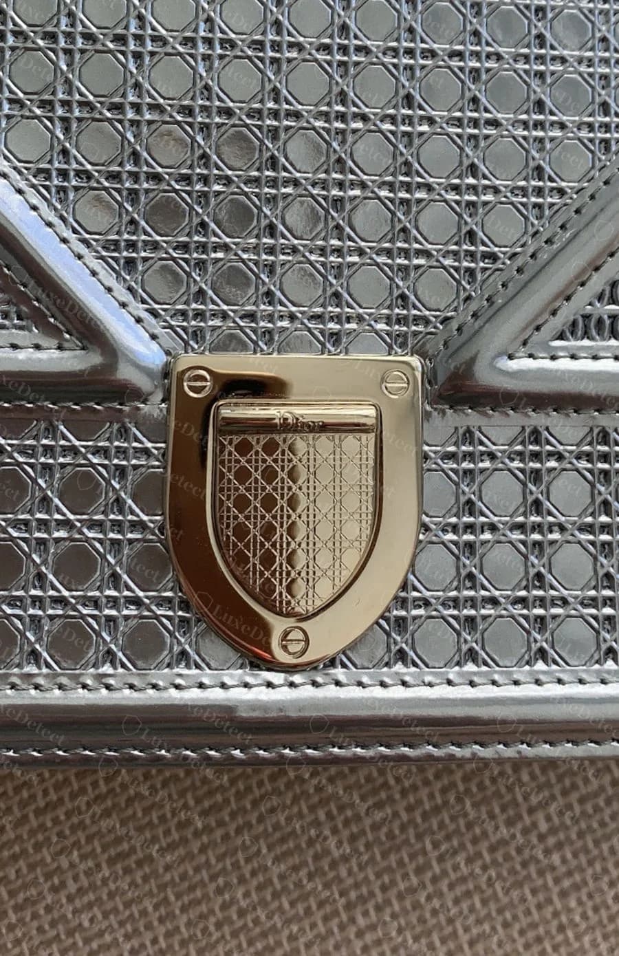 Dior Diorama in mirrored metallic leather, close on the CD clasp plate where the stamped micro-cannage carries through cleanly across both the plate and the surrounding panel