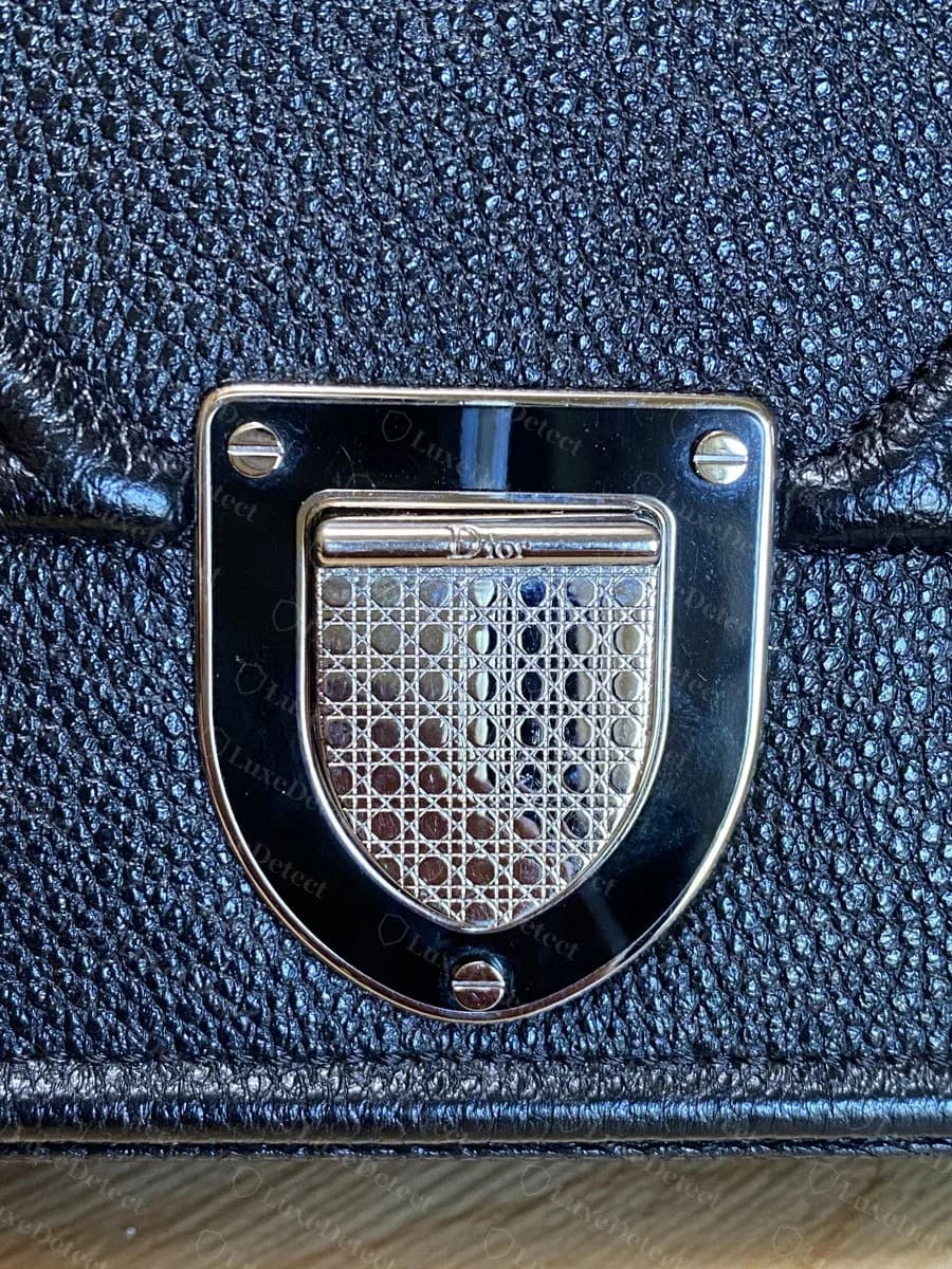 Dior Diorama micro-cannage clasp plate on black grained leather, showing the stamped dot-and-cross-hatch pattern and the four corner screws