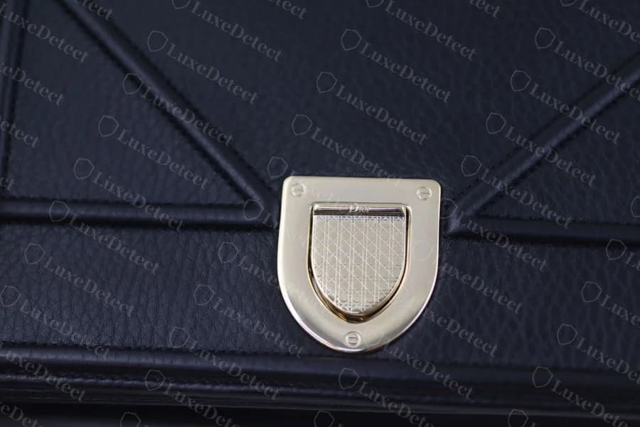 Dior Diorama CD clasp on navy grained leather, showing the D-shaped lock, the Dior wordmark on the horizontal bar, and the four corner screws seated flush against the plate