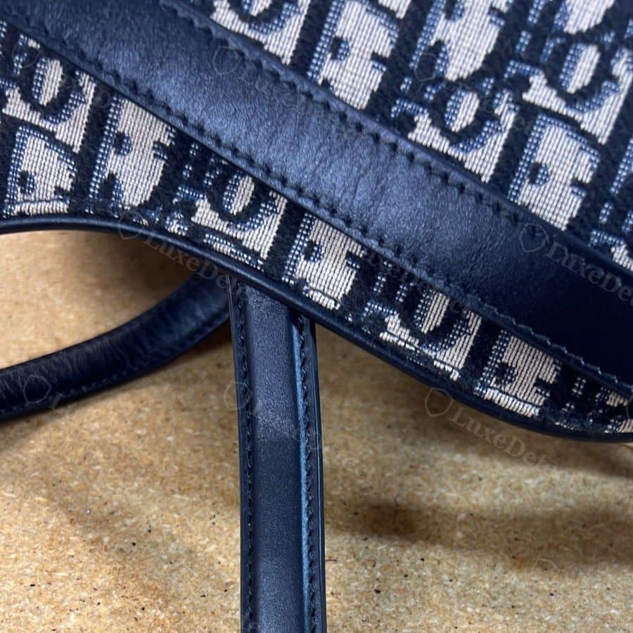 Counterfeit Oblique canvas at a strap seam: pattern and weave look plausible in isolation, which is why a seam-by-seam check matters more than a single photo