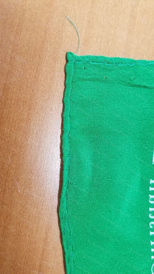 Counterfeit scarf edge from our sample: a machine-serged, overlocked zigzag stitch finishing a raw cut edge, not a rolled hem