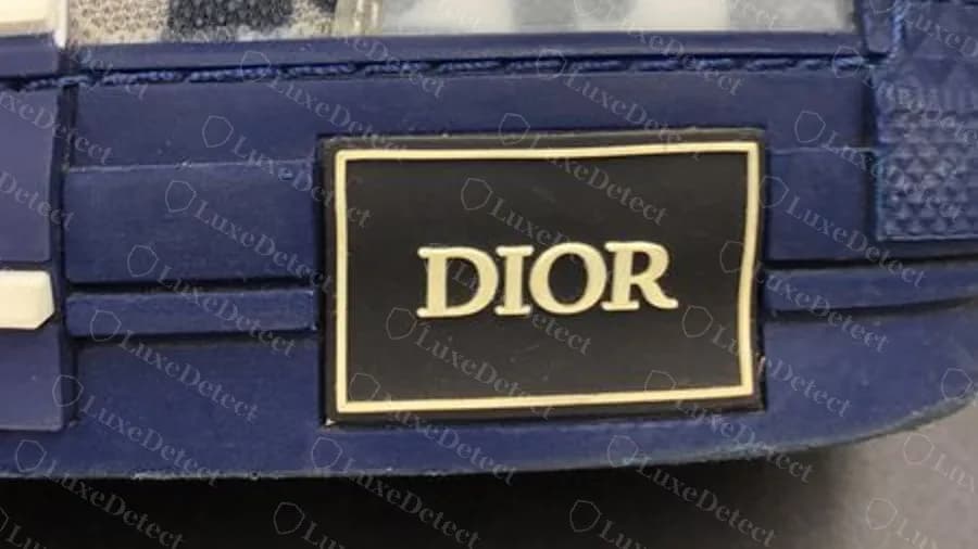 Genuine Dior B23 heel plate, a black rectangular plate with a gold border and DIOR in gold serif capitals, set into the navy rubber heel counter