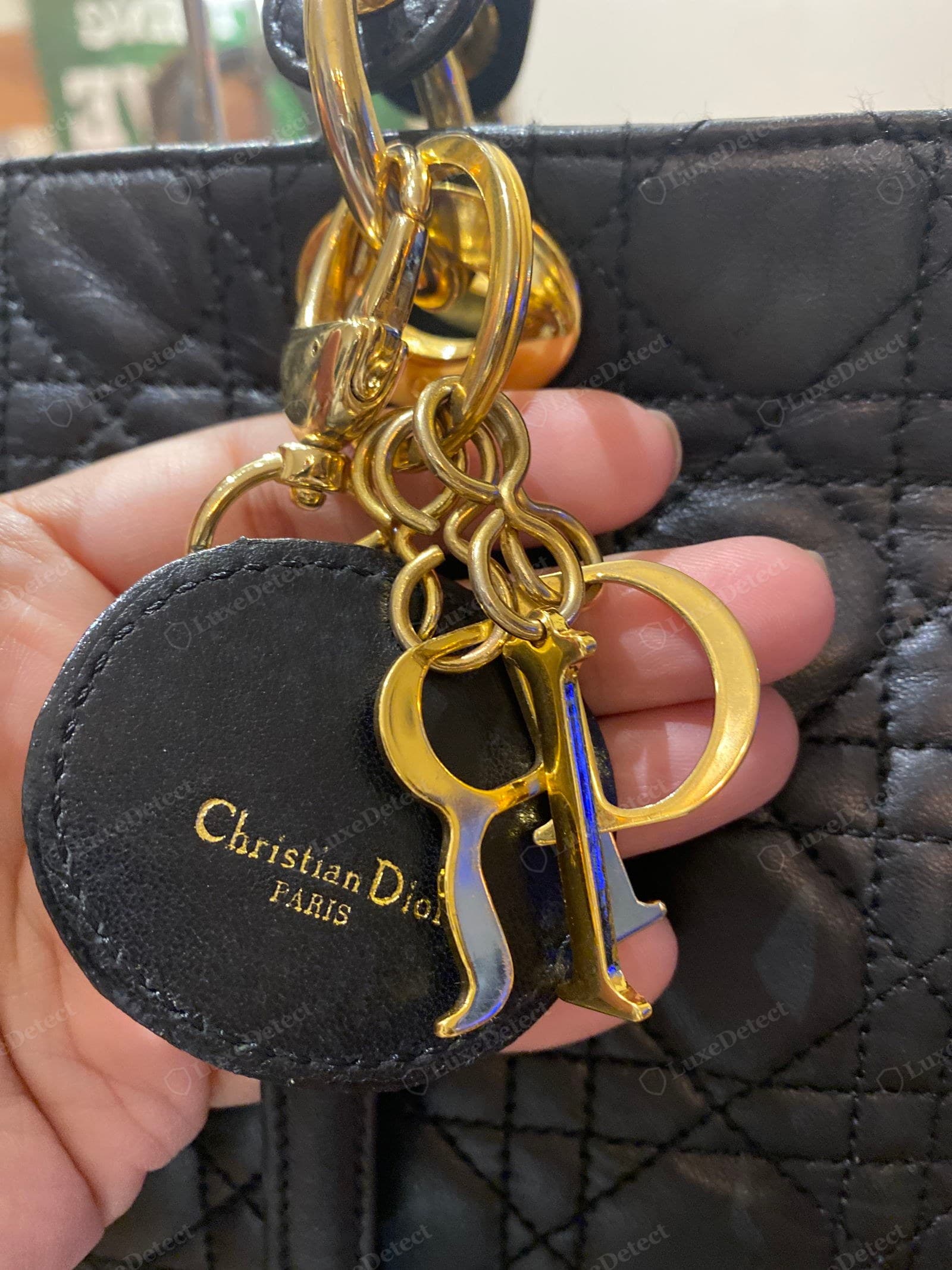 Counterfeit Lady Dior charms — bright brassy gold letters with a blue-tinted discolouration and slightly wrong letterforms, hanging from a round "Christian Dior PARIS" leather medallion the genuine bag does not use, over an over-tight small-scale cannage