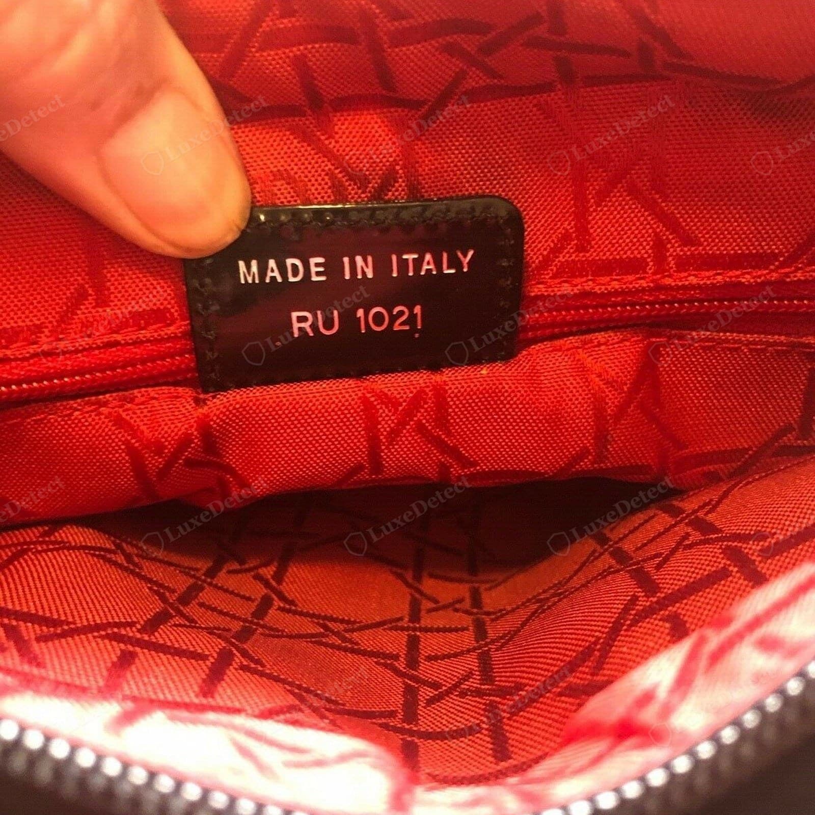 Genuine Lady Dior interior code tab — a black patent leather tab heat-stamped in white "MADE IN ITALY / RU 1021" (the production code), tucked into a seam against the red "Christian Dior" cannage-jacquard lining