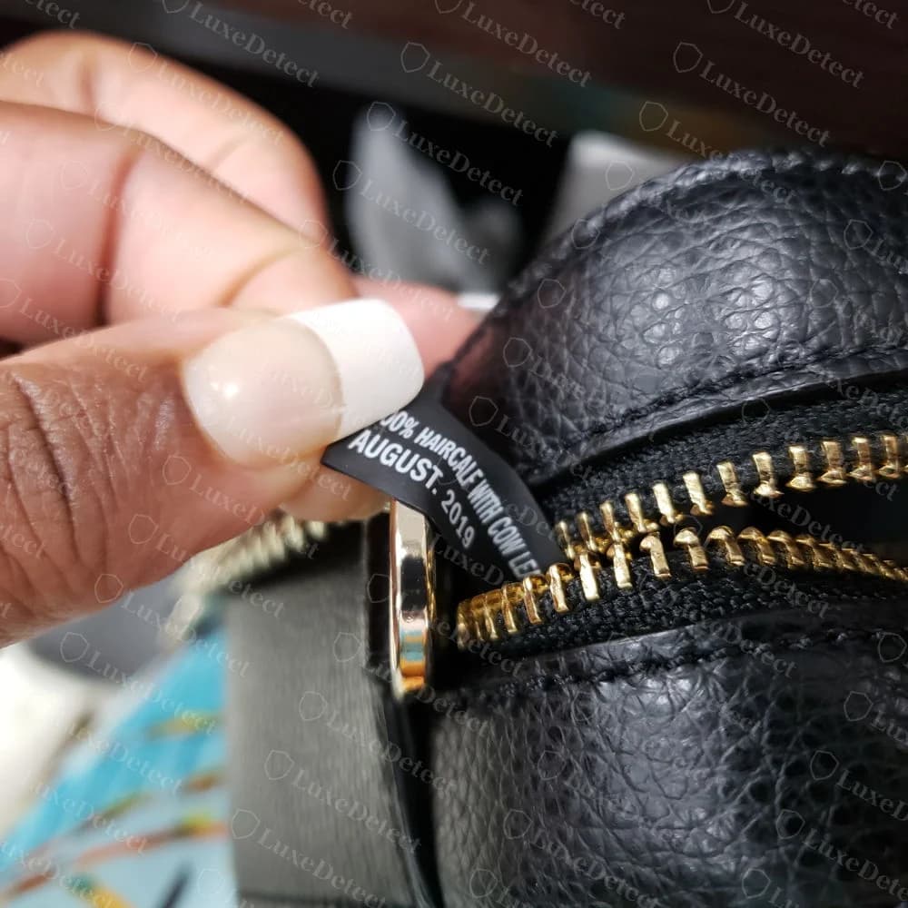 Genuine DKNY black care label with a material line and AUGUST. 2019, sewn beside a zip on a black pebbled-leather bag