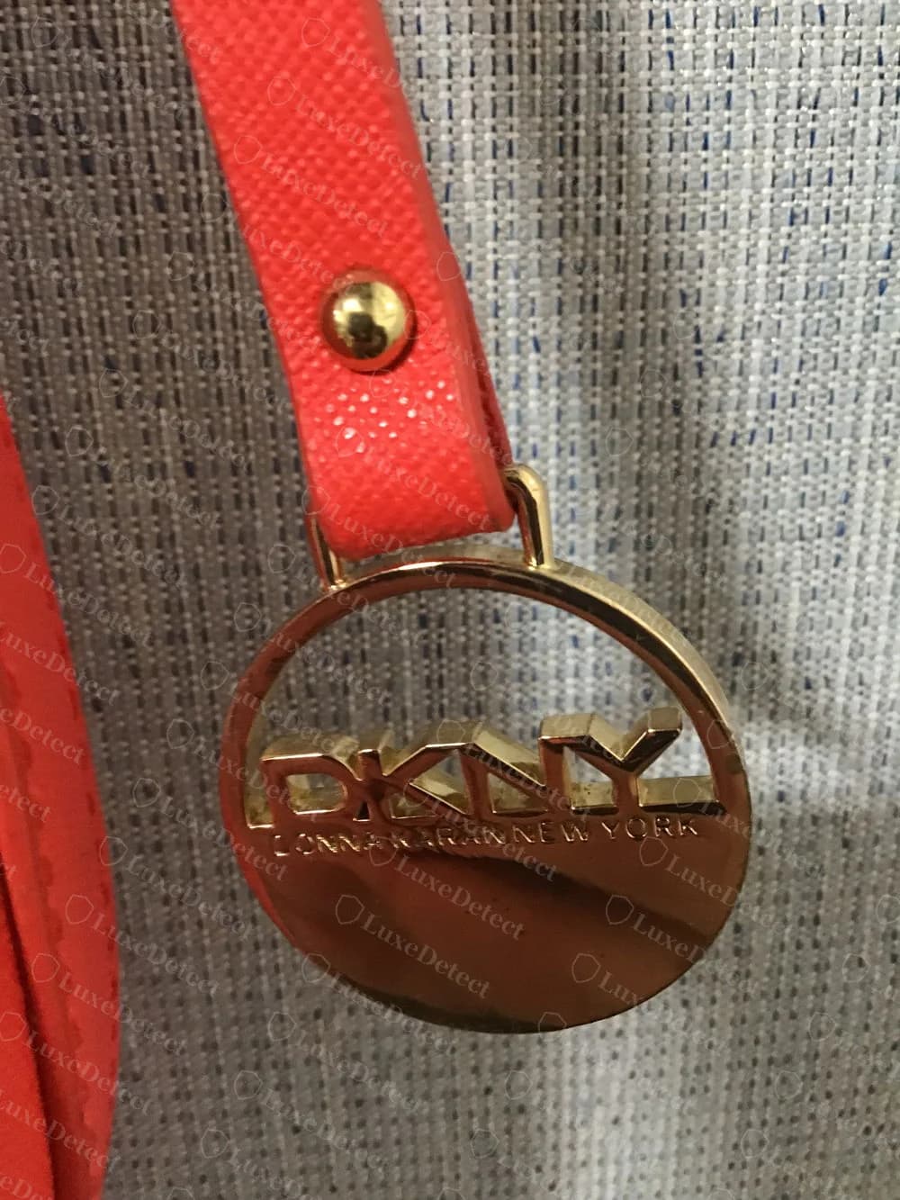 Genuine DKNY gold-tone round charm hanging from a red saffiano strap, with DKNY cut out across the circle and DONNA KARAN NEW YORK around the lower edge