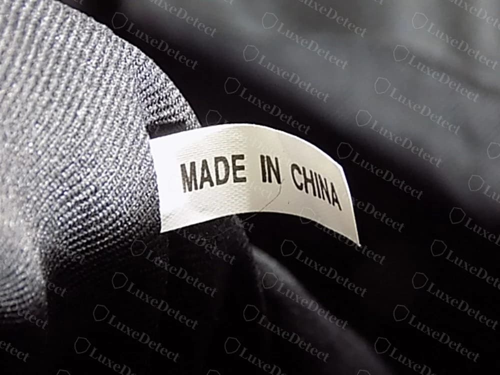 Pequeña etiqueta interior blanca original de DKNY en tejido satinado que dice MADE IN CHINA, colgando de una costura en un bolso de tela oscura