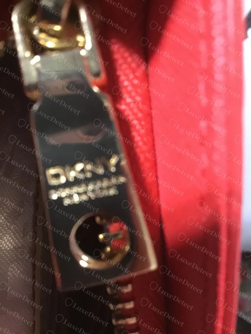 Tirador dorado original de cremallera de DKNY con DKNY estampado y Donna Karan New York debajo, un orificio redondo para el tornillo cerca de la base, fotografiado ligeramente desenfocado