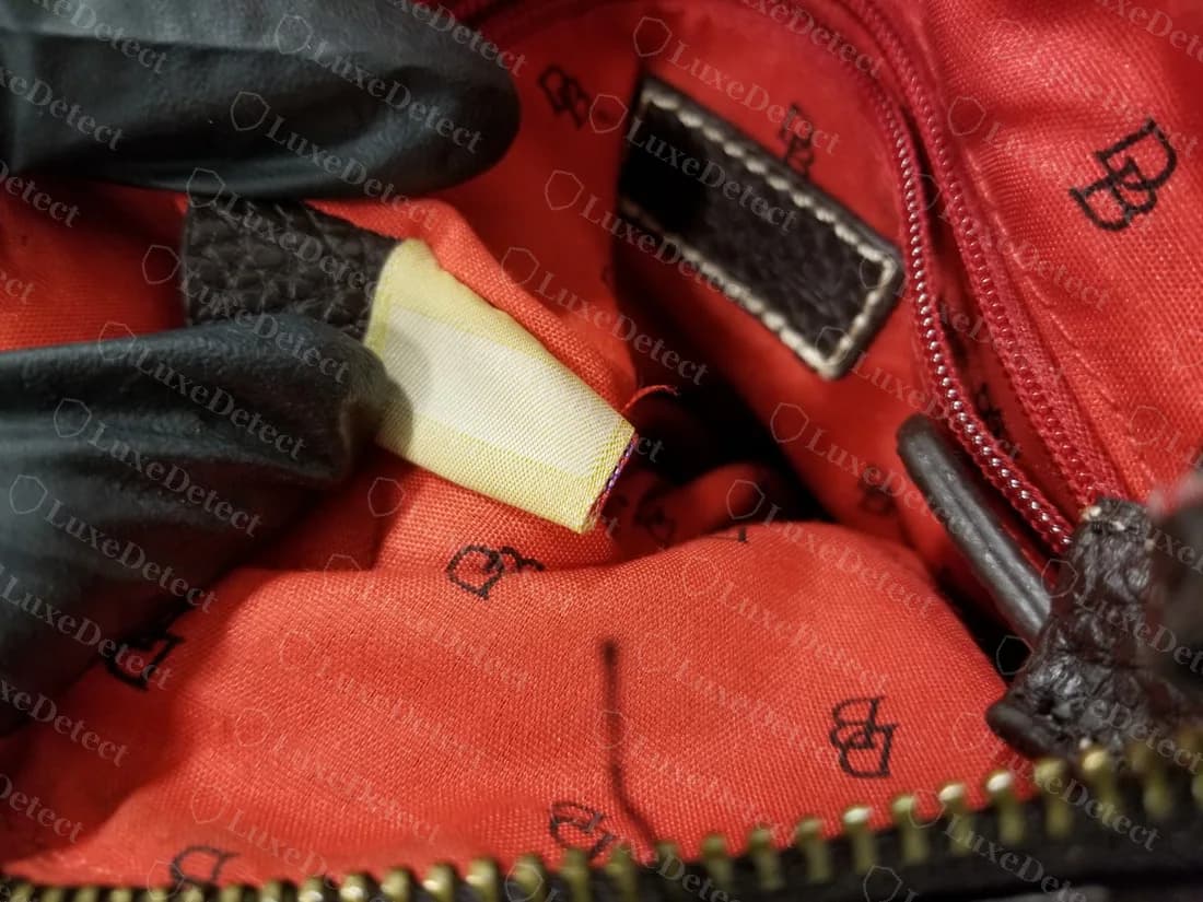 Bolso Signature falso: la etiqueta de registro sacada de la costura muestra un panel pálido en blanco sin número, sobre un forro rojo estampado con logos DB dispersos