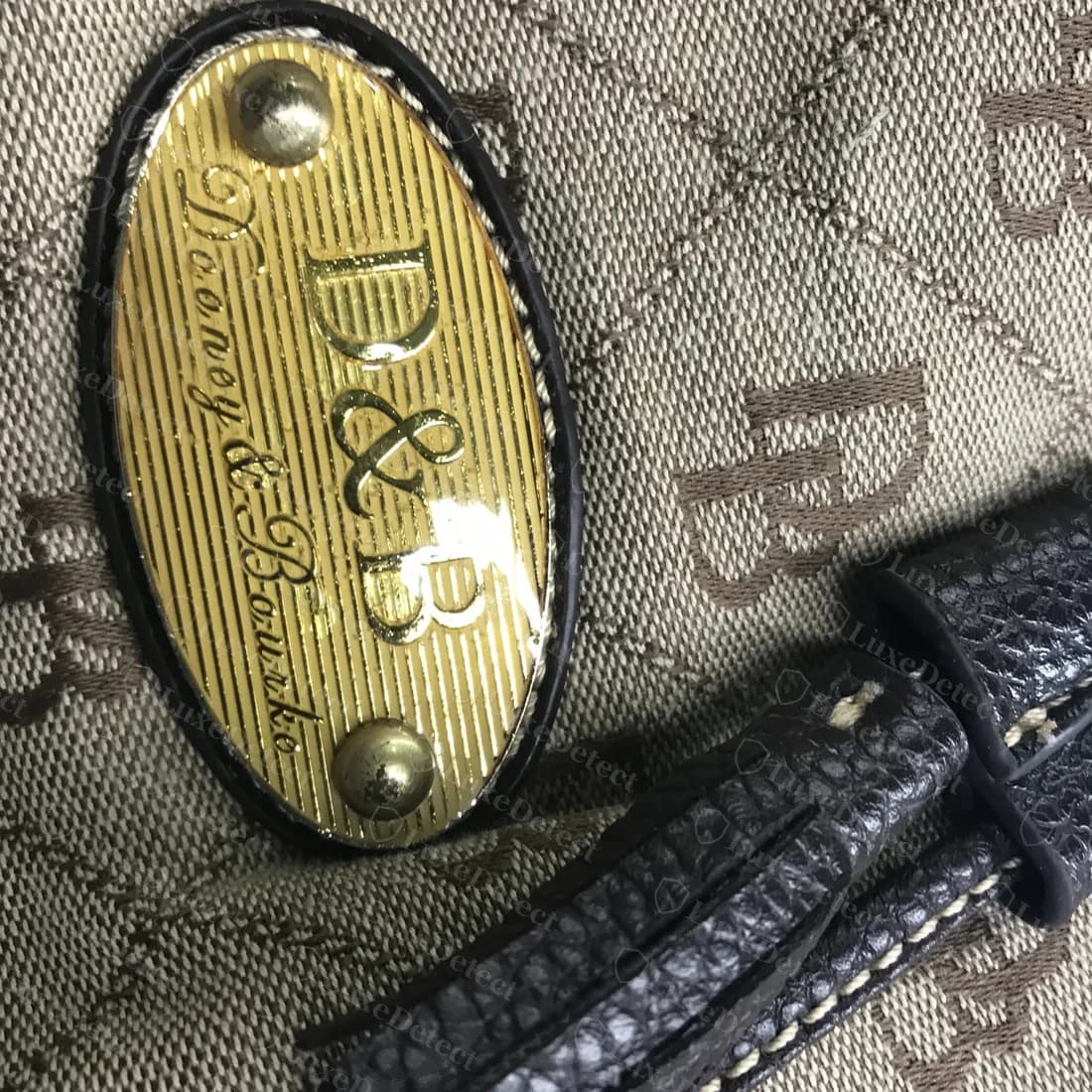 Placa falsa: una placa ovalada de latón rayada con un monograma "D&B" grande sobre letras en cursiva deformes, en un bolso de jacquard