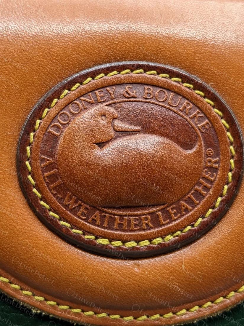 Echter Entenpatch einer Vintage-All-Weather-Leather: ein geprägtes Oval mit DOONEY & BOURKE ALL-WEATHER LEATHER rund um die Ente, mit gelbem Garn aufgenäht