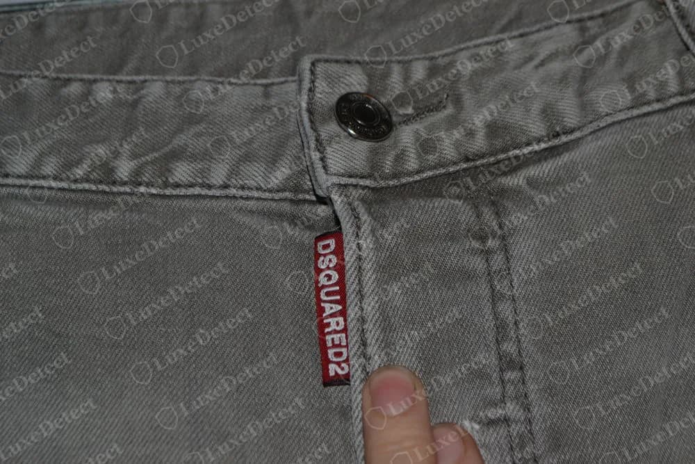 Genuine Dsquared2 grey jeans: engraved metal button above a red woven fly tab reading DSQUARED2 in white capitals, running down the fly