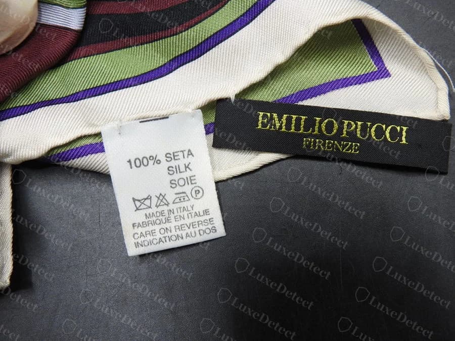 Genuine Emilio Pucci silk scarf corner showing a black and gold woven label reading EMILIO PUCCI FIRENZE beside a small white care tag reading 100% SETA SILK SOIE, MADE IN ITALY