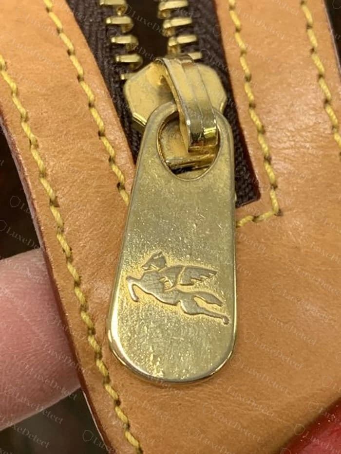 Puxador de zíper dourado em formato de gota Etro original gravado com um cavalo alado, em uma aba de zíper de couro caramelo ao lado de lona paisley marrom