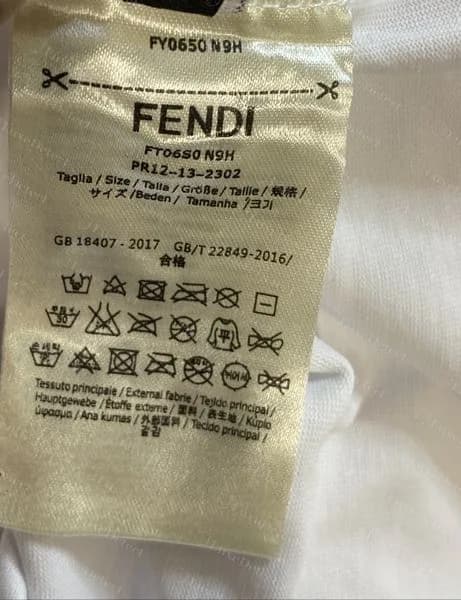 Etiqueta de cuidado de una camiseta Fendi falsificada: el código de estilo impreso dos veces con caracteres distintos, una línea de cumplimiento GB 18407 - 2017 y sin bloque de composición ni de país de fabricación