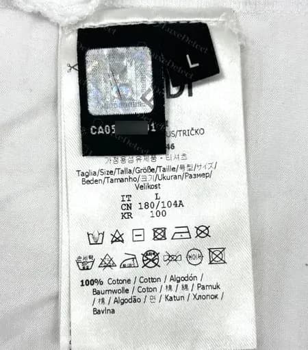 Genuine Fendi T-shirt side-seam stack: a black tab with a silver FF hologram and a printed CA number, a separate black size tab beside it, both sewn in with the white care label