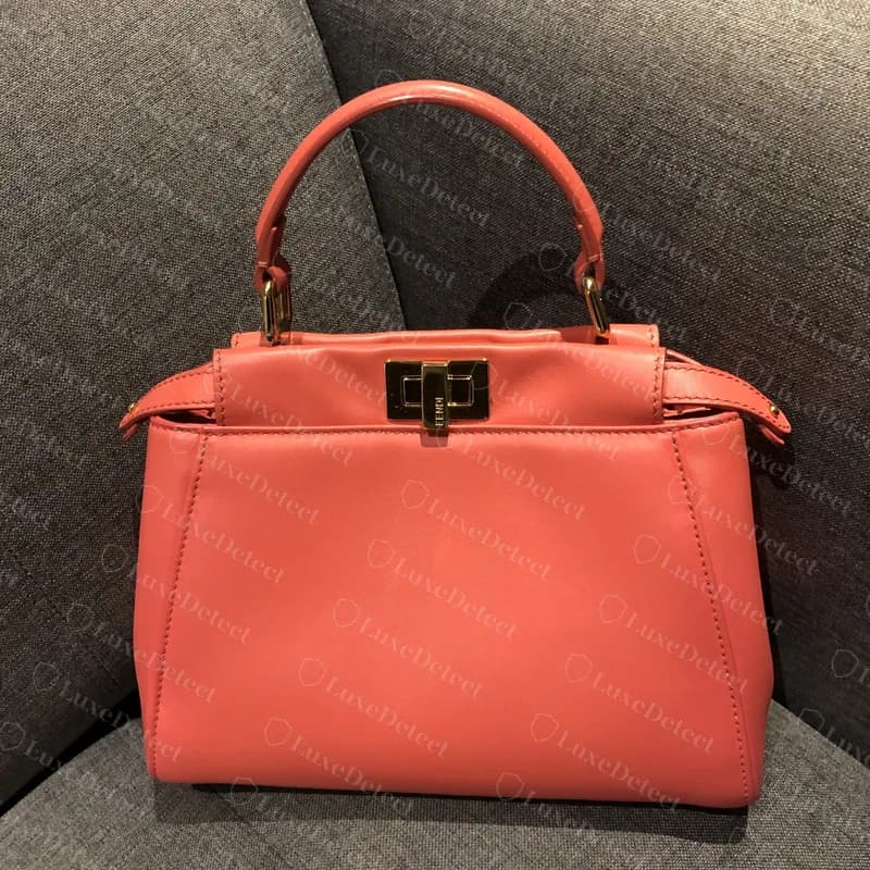 Genuine small Peekaboo in coral smooth calf, front view: a rolled top handle, a turn-lock on the flap and a trapezoid body with side tabs