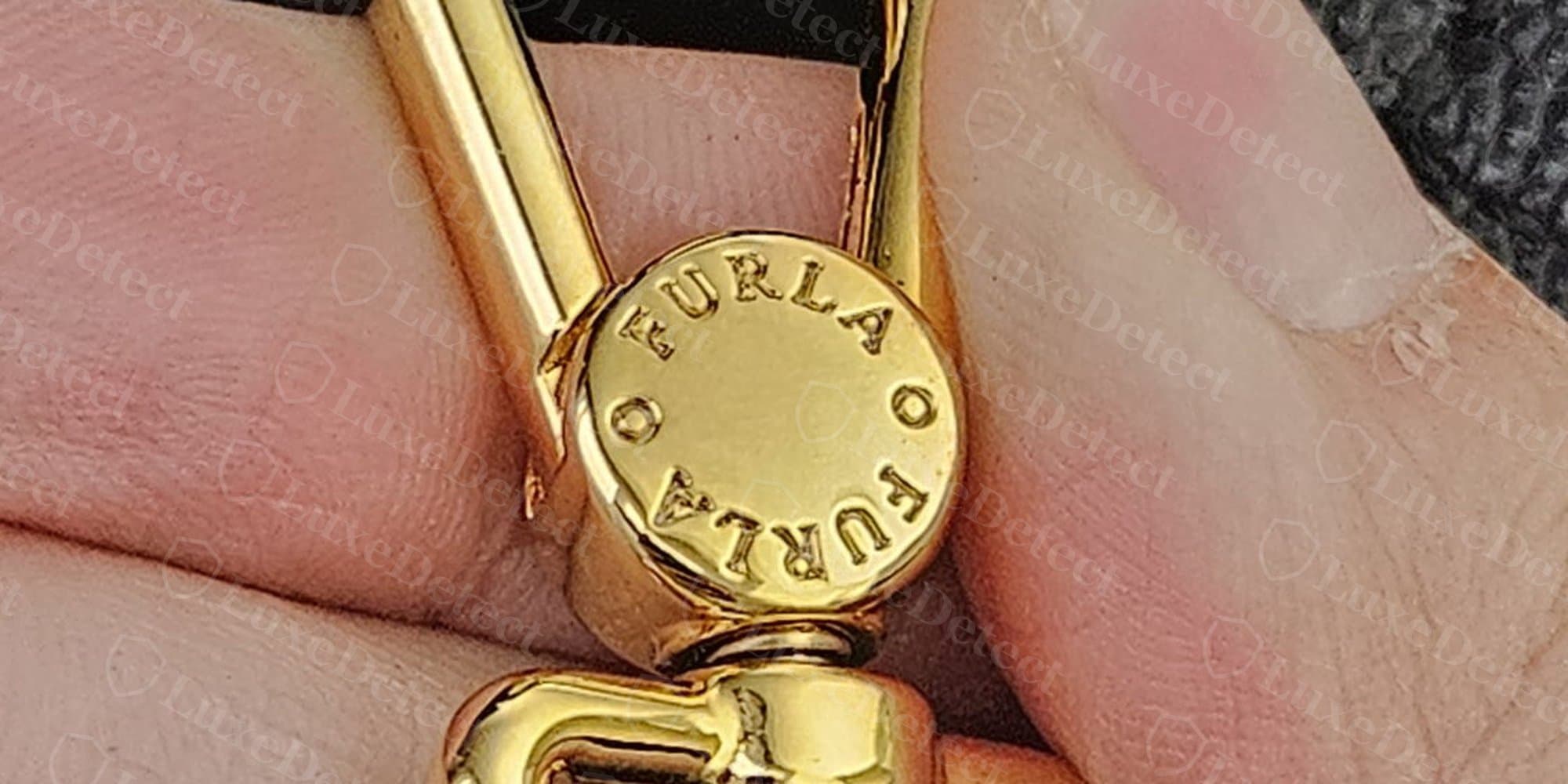 Genuine swivel-hook hardware with a repeating "O FURLA O FURLA" engraving around the rivet head, crisp and evenly spaced.