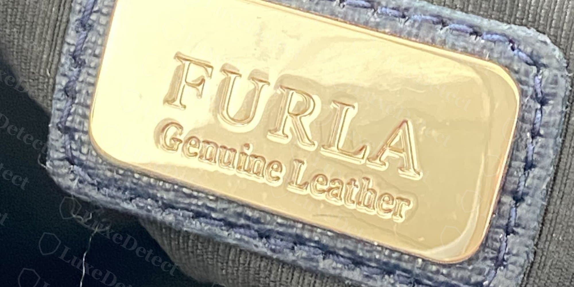 Authentic interior tag: gold-foil "FURLA / Genuine Leather" on a metal plate stitched into a leather surround.
