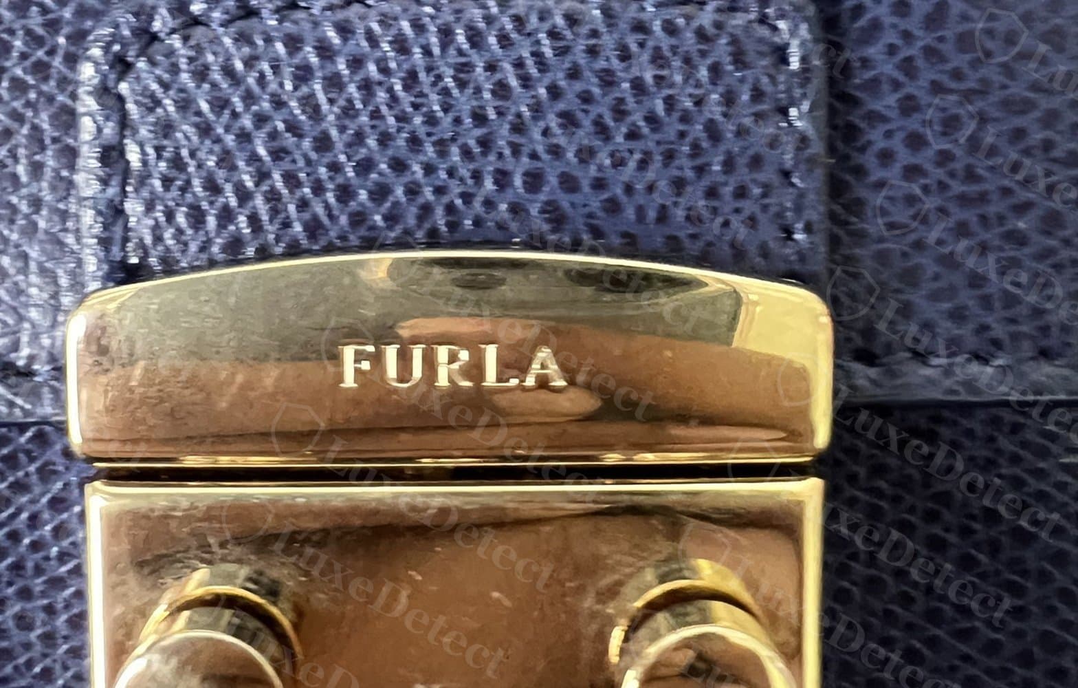 Genuine Furla turn-lock, front view: deeply engraved "FURLA" wordmark on an even, high-gloss gold plate with visible screw posts above.