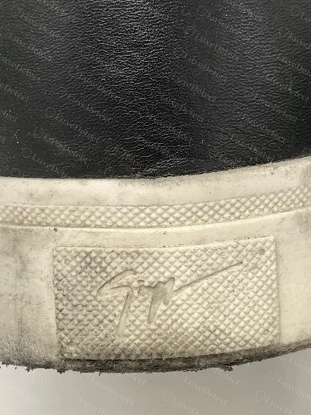 Ferse eines echten Giuseppe Zanotti mit einem strukturierten Gummipatch, in den die Signatur eingeformt ist, hinten an einer weißen Sohle, unter schwarzem Leder