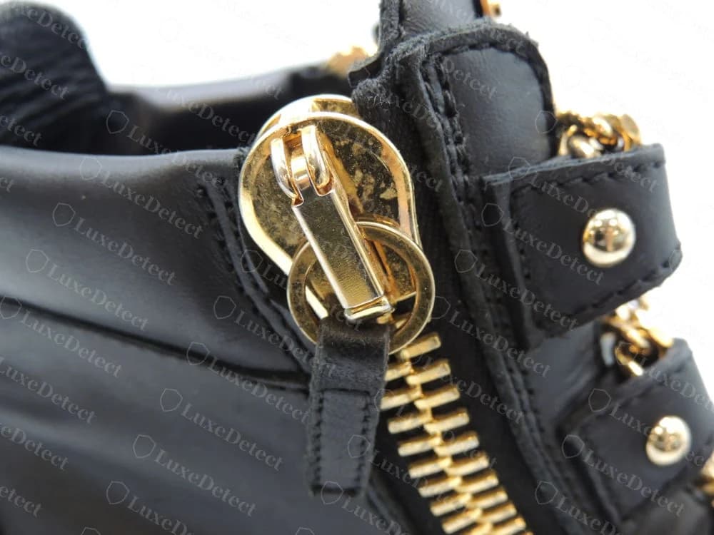 Cremallera trasera de una zapatilla alta con cadena London original de Giuseppe Zanotti con un cursor dorado, una anilla partida y una lengüeta de piel negra junto a tachuelas doradas