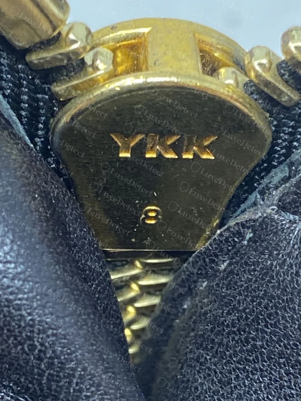 Echter goldfarbener Giuseppe Zanotti Zipper mit der Prägung YKK und der Zahl 8, zwischen schwarzen Lederteilen gesehen
