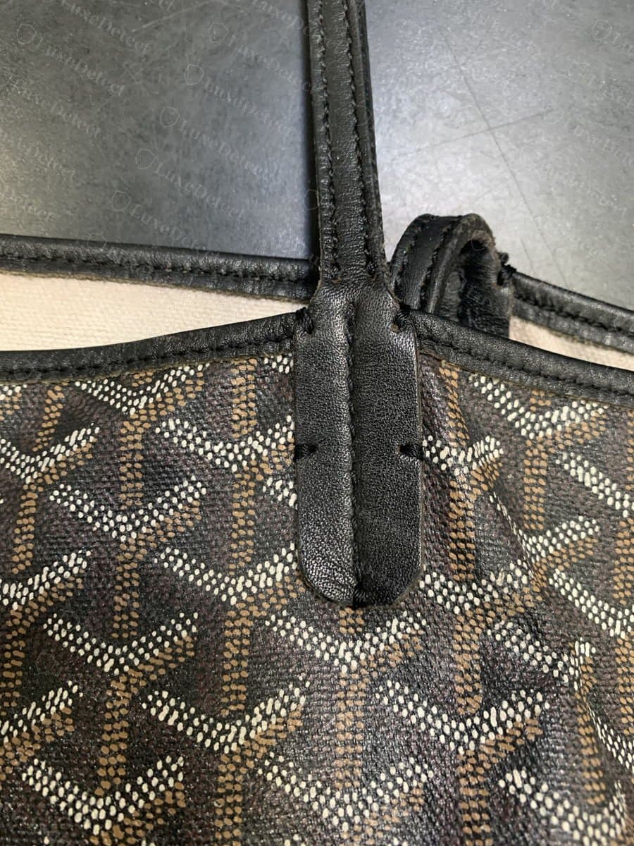 Fixation d'anse authentique sur un Goyard Saint Louis noir : la languette de cuir repose sur le corps du sac et les chevrons Goyardine se poursuivent autour