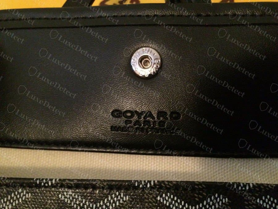 Faux : l'estampille Goyard Paris Made in France sur le rabat d'une pochette noire, avec des lettres épaisses et grasses sous le bouton-pression